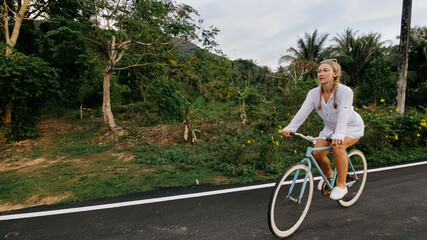 Biking road trip. The woman on blue bike in white clothes on forest road. The girl ride on bicycle. Cycling Cycle Fix. Asia Thailand ride tourism. Take a photo with a bike.