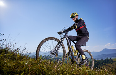 Fototapeta na wymiar Joyful male cyclist riding bicycle uphill under blue sky.
