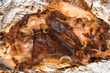 baked meat and fried onions on a baking sheet, pork ham on foil and wooden background, home cooking