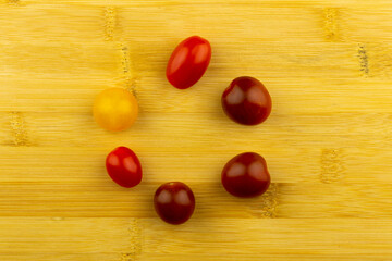 Small colorful tomatoes stacked on a wooden chopping board. Artificial light from two lamps, soft shadows