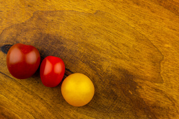 Small colorful tomatoes stacked on a wooden chopping board. Artificial light from two lamps, soft shadows