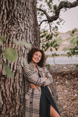 Nice girl with curly hair under an oak tree. Spring, autumn. Blue sky with clouds. 