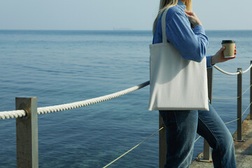 Woman with paper cup and eco bag standing on the pier against sea