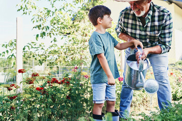 Happy grandfather with grandson watering vegetables in the garden.