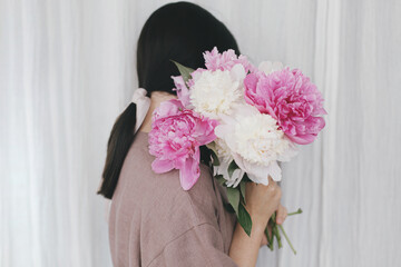 Stylish woman in linen dress holding peony bouquet at white fabric. Slow life. Aesthetic moment