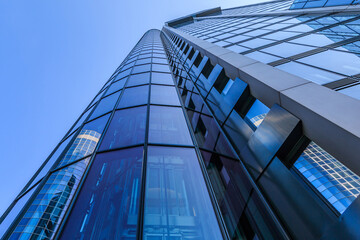 Glass facade of a high-rise in Frankfurt. View along one of a skyscraper with reflections in the windows. House of the finance and business district with blue sky and sunshine