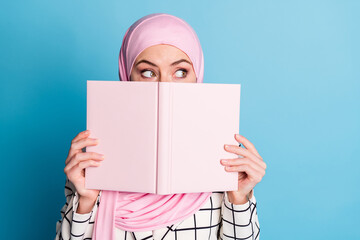 Close-up portrait of funny curious muslimah girl closing face book looking aside isolated over...