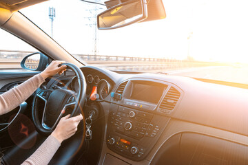 Obraz premium Happy driver inside car at sunset. Young woman have fun ride trip travel on road in winter sunny day. Drive vacation concept.