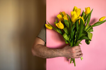 A man's hand holds a bouquet of yellow tulips on a pink background. Unexpected surprise.