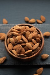Almonds nuts close-up in a round wooden cup on a black shabby chic board on a black schiffer 
 background.Nuts and seeds. .Healthy fats.Heap Almonds shelled  nut closeup.Tasty organic snack 