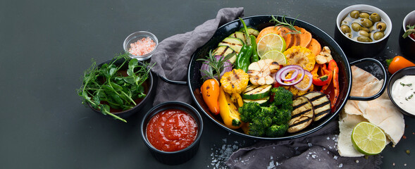 Grilled assorted vegetables in cast iron pan on black background.