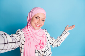 Self-portrait of pretty cheerful muslimah girl demonstrating copy space advice isolated over bright...