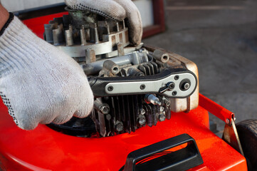 The man is repairing the mower in the garage. He tightens the candle.