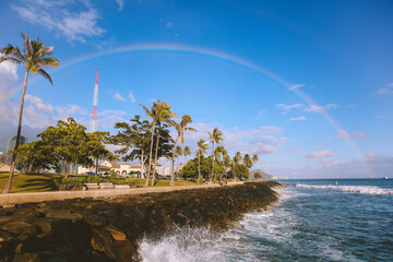 Rainbow at Kakaako Waterfront Park, Honolulu, Oahu, Hawaii. waves hitting rocks. plam trees