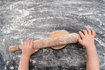 Child rolling out dough on flour table. Top view.
