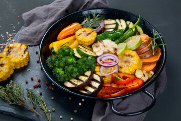 Grilled assorted vegetables in cast iron pan on black background.