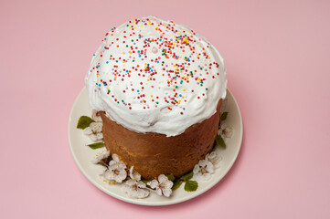 Easter composition. Glazed Easter cake decorated with sugar sprinkles and apricot flowers on a white plate close-up on a pastel pink background. Happy Easter Holidays. Side view. Selective focus.