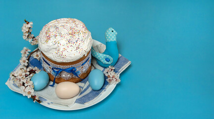 Easter composition. Eggs, apricot flowers, a cute handmade bird and a glazed Easter cake decorated with sugar sprinkles on a blue background. Happy Easter Holidays. Side view. Free space.