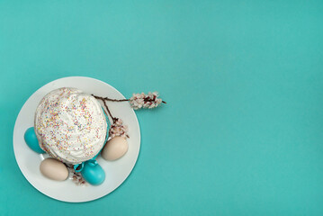 Easter composition. Eggs, apricot flowers and a glazed Easter cake decorated with sugar sprinkles on a white plate close-up on a blue-green background. Happy Easter Holidays. Top view. Free space.