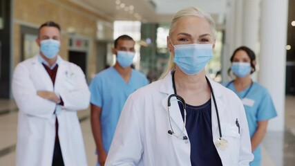 Satisfied senior doctor wearing face mask with team in background - Powered by Adobe