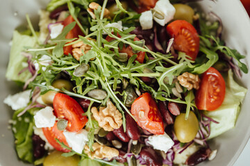 Healthy fresh salad of vegetables, cucumber, tomato, spinach, arugula and olives and cheese in a plate on a white table, pumpkin, walnut and sunflower seeds. From above close up, raw food concept
