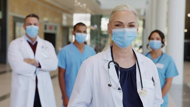 Satisfied senior doctor wearing face mask with team in background