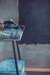 Denim jeans and headphones at stool or shelf near grey wall background texture.  Stack of jeans