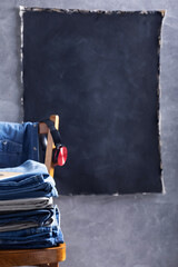 Denim jeans and headphones at old wooden chair near grey wall background texture.  Stack of jeans