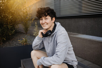 Junge sportliche Person sitzt mit Kopfhörern auf einer Treppe in urbaner Umgebung 