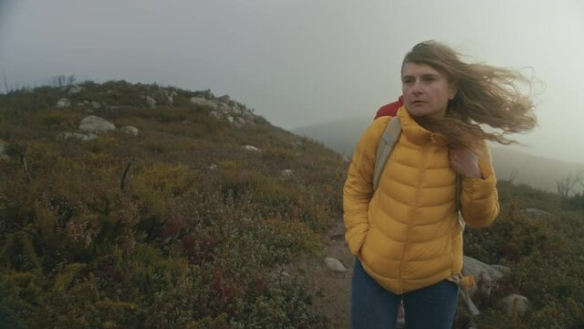 Cinematic moody couple walk on top of windy mountain top during difficult hike. Serious tourists, lost on high altitude. Wind blows woman hair. Explore new territory, outdoors vibes lifestyle