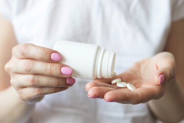 Woman pouring pills from jar into her hand, taking pills, medicine concept
