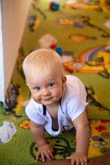 Fototapeta na wymiar Beautiful blonde toddler crawls on all fours on the floor in summer and smiles very cute