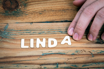 LINDA. Name of women and girls. White letters of the alphabet on a wooden background