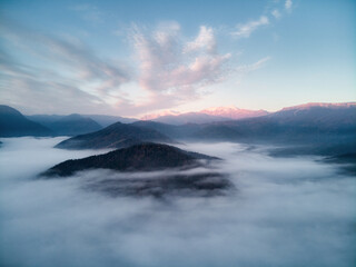Aerial view, sea of fog and clouds illuminated by the rising sun, snow on the tops of the mountains. Russia