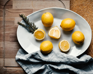 Lemons whole and cut in half, on a white plate, on wooden background