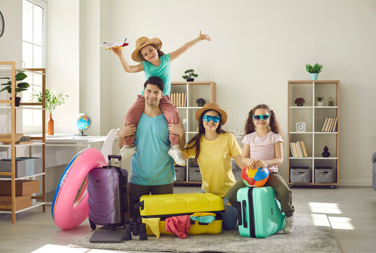 Portrait of happy family with daughters looking at camera ready to fly to tropical resort. Father and mother with little girls children having fun at home sitting on home floor next to travel luggage