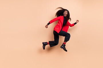 Fototapeta na wymiar Photo of sweet cute curly dark skin woman dressed red blazer jumping running looking back empty space isolated beige color background