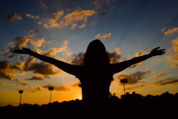 Silhouette of a young woman with arms up, celebrating life at sunset