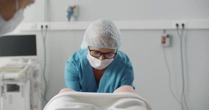Obstetrician in safety cap and mask assisting woman in labor