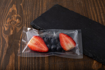 Fresh blueberries and strawberries in vacuum sealed plastic bag on wooden table