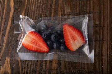 Fresh blueberries and strawberries in vacuum sealed plastic bag on wooden table