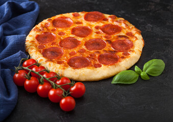 Fresh round baked Pepperoni italian pizza with tomatoes with basil on black background with blue linen towel.