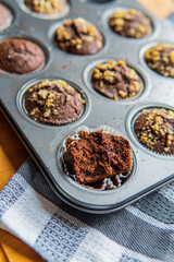 Selective focus on a half eaten healthy gluten free chocolate muffin with walnuts. Homemade, freshly baked goods with cocoa powder and dark chocolate placed in a muffins tray in the background.