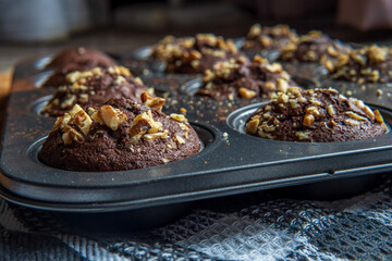 Close up on healthy gluten free chocolate muffins with walnuts. Homemade, freshly baked goods with cocoa powder and dark chocolate placed in a muffin tray on a wooden background. Nutrition concept.