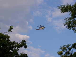 Fototapeta na wymiar Police helicopter flying in the blue sky during the day, tree branches on the edges, side view