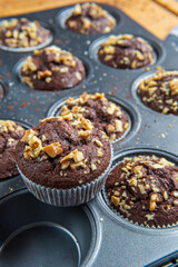 Close up on a healthy gluten free chocolate muffin with walnuts. Homemade, freshly baked goods with cocoa powder and dark chocolate placed in a muffins tray on a wooden background. Nutrition concept.