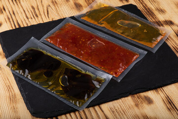 Different sauces in vacuum sealed plastic packaging on black slate