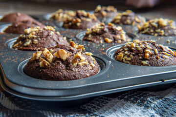 Healthy gluten free chocolate muffins with walnuts. Homemade, freshly baked goods with cocoa powder and dark chocolate placed in a muffin tray on a wooden background. Nutrition concept, side view