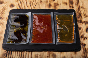 Different sauces in vacuum sealed plastic packaging on black slate