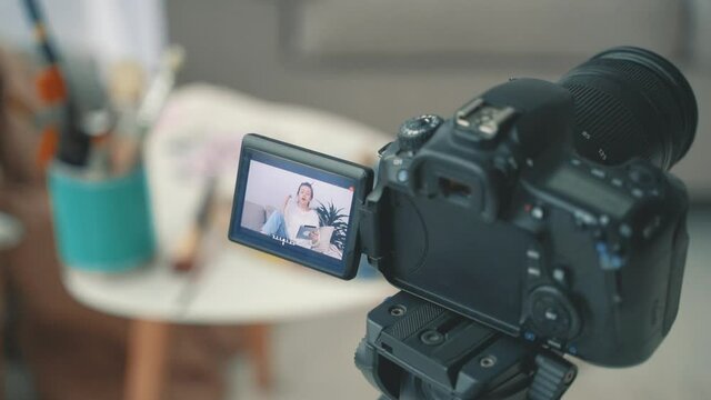 Camera recording a video tutorial close-up. Streamer at home. Young female artist explaining her illustration.